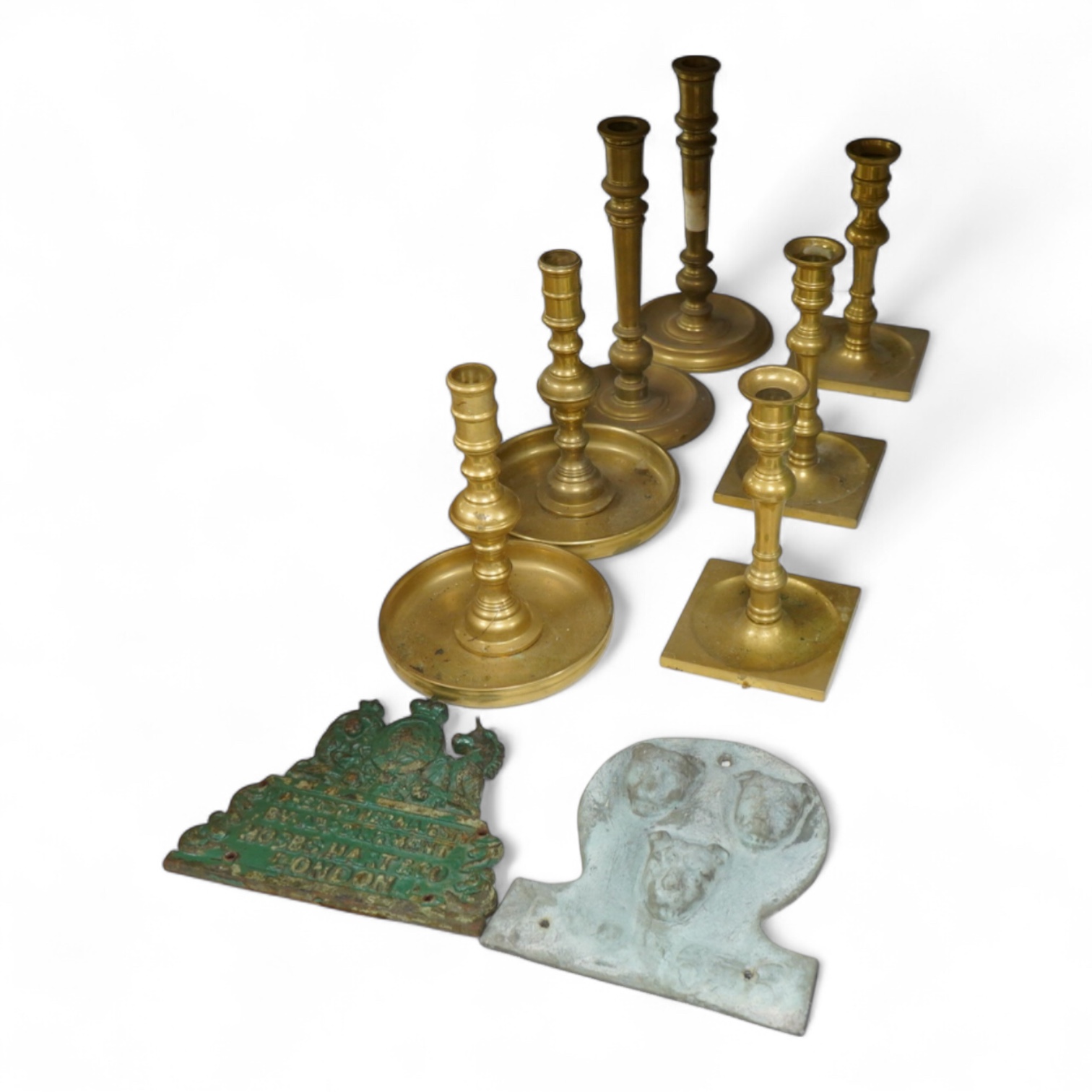 Two fire marks and a collection of brass candlesticks, tallest 25.5cm